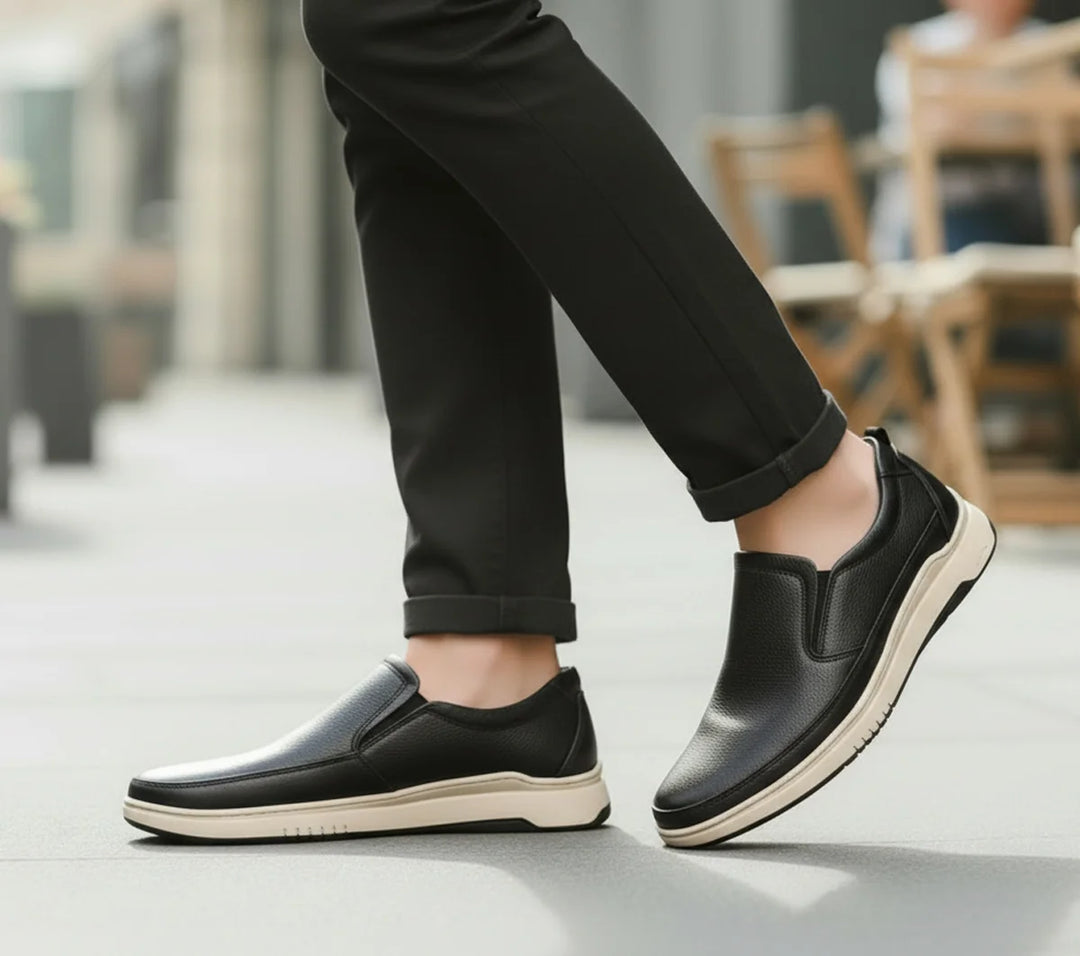 Person wearing black slip-on shoes with white soles on a blurred outdoor background