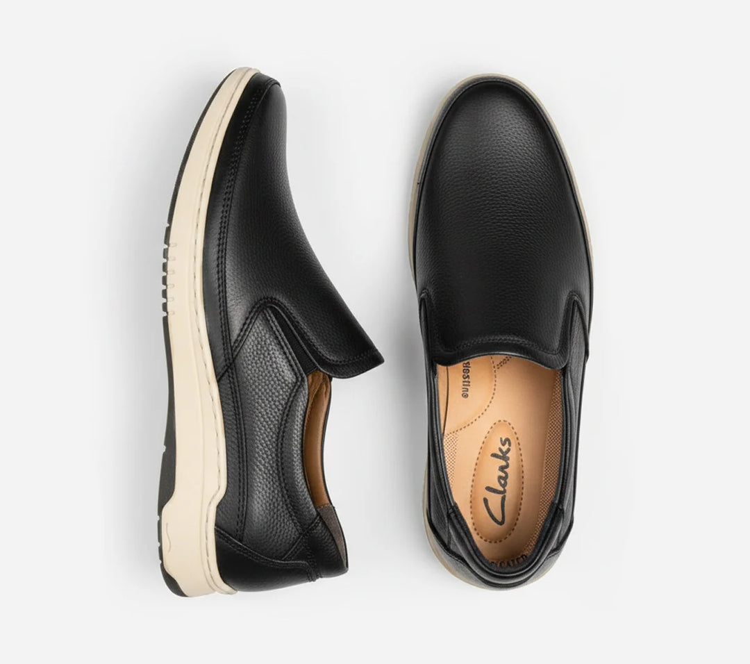 Pair of black slip-on shoes with white soles on a light gray background