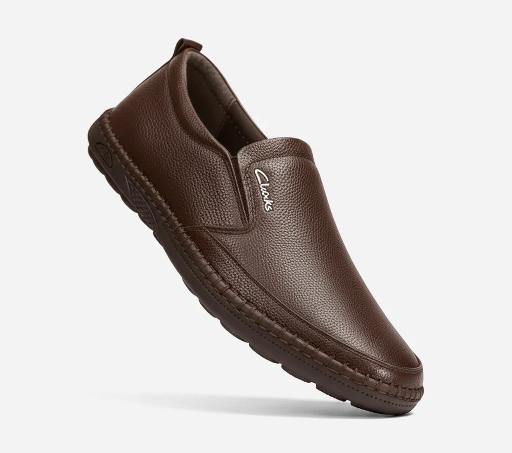 Brown leather slip-on shoe with Clarks logo on a light gray background
