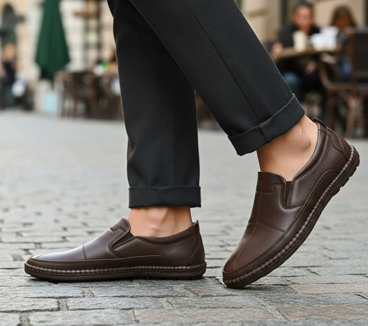 Brown loafers worn with black pants on a cobblestone street.