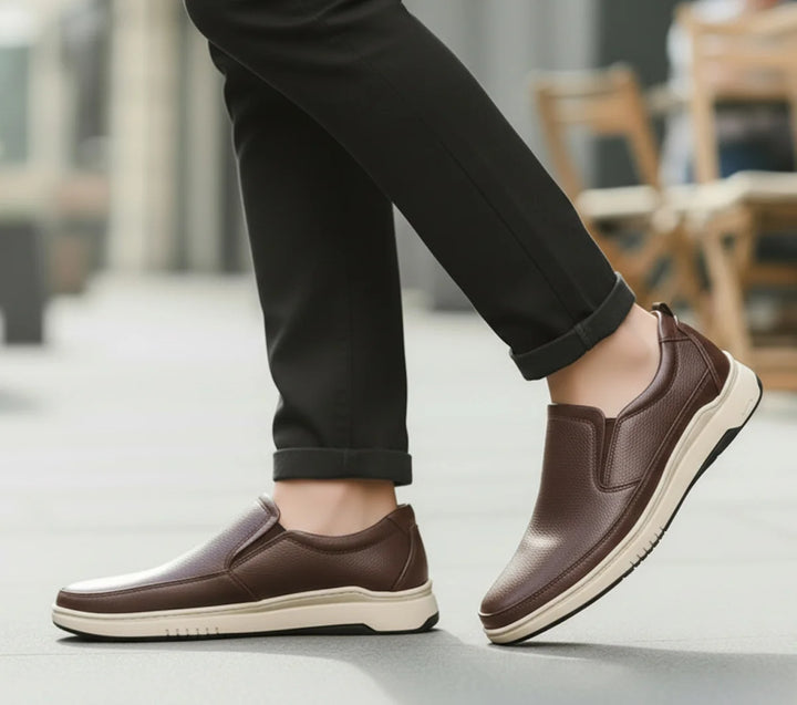 Brown slip-on shoes worn with black pants on a blurred outdoor background