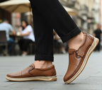 Brown loafers worn on a city street with blurred people in the background